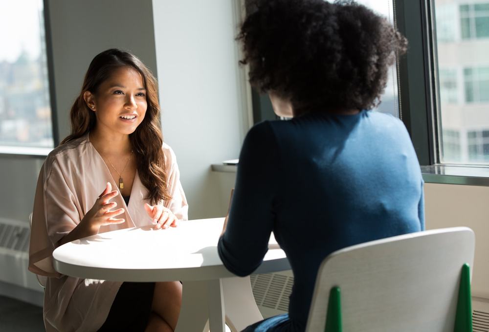 Two people talking across a table in a bright office during an interview